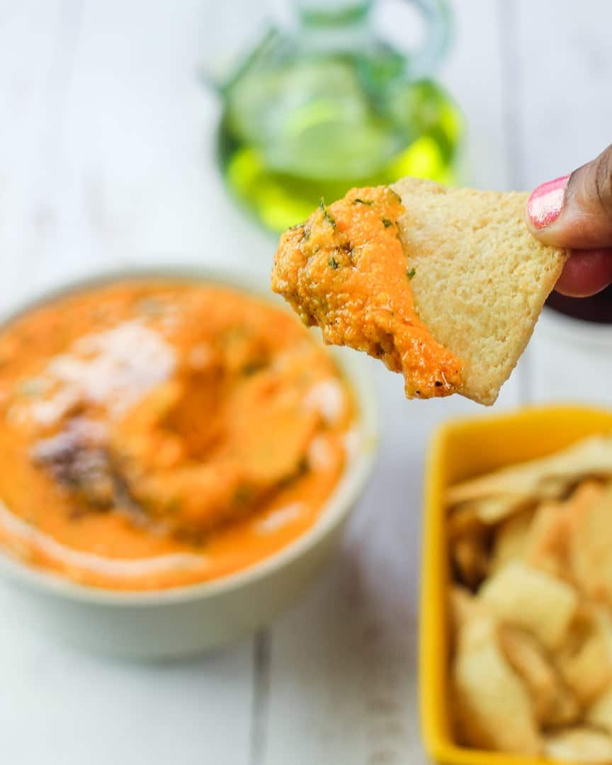Hand scooping up carrot hummus on a pita chip. 