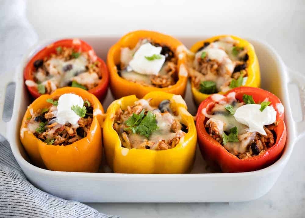 5-ingredient chicken stuffed peppers in a baking dish with melted cheese, cilantro and dollops of sour cream on top. 