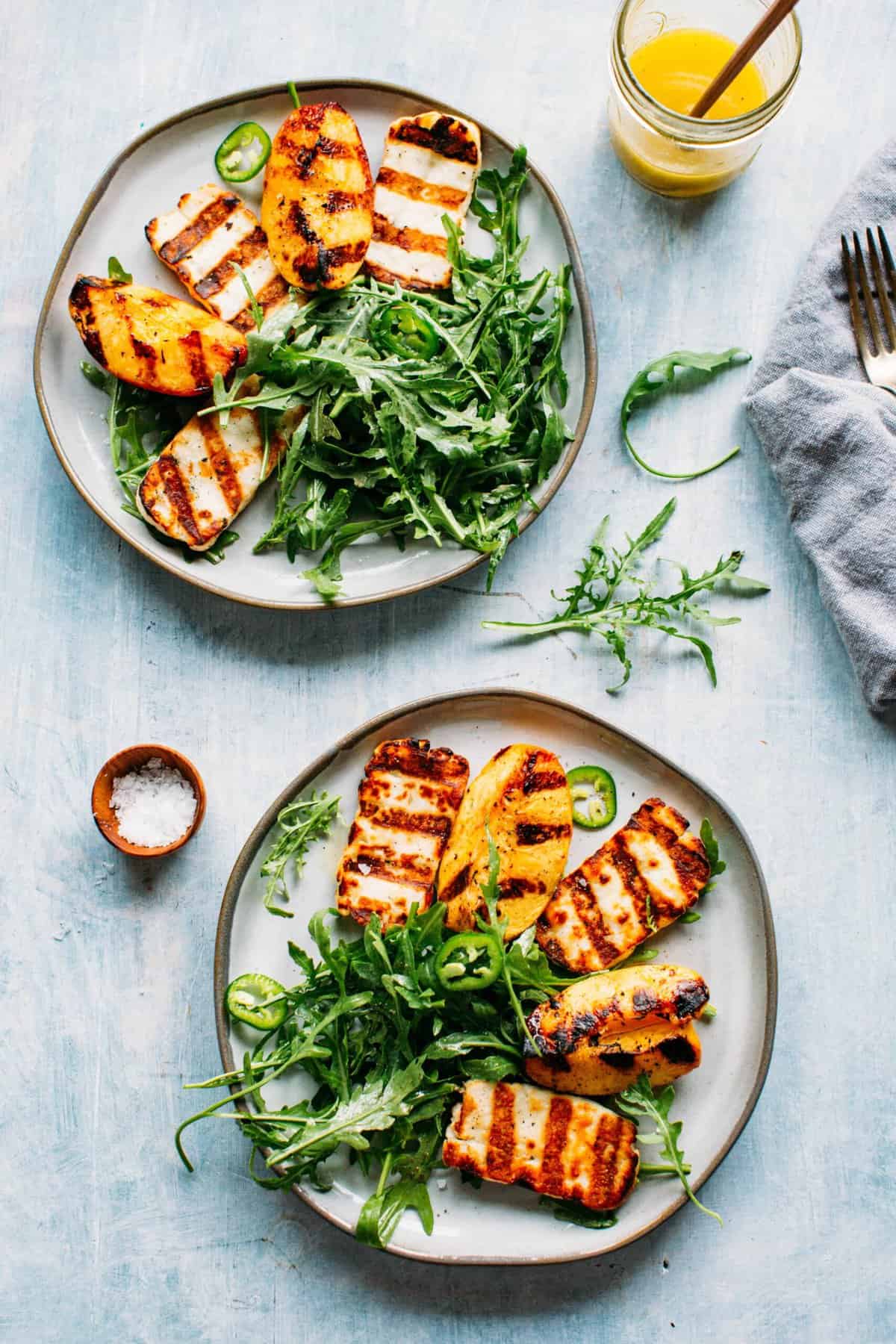 Grilled halloumi + peaches with an arugula salad on a plate and a small mason jar of dressing on the side. 