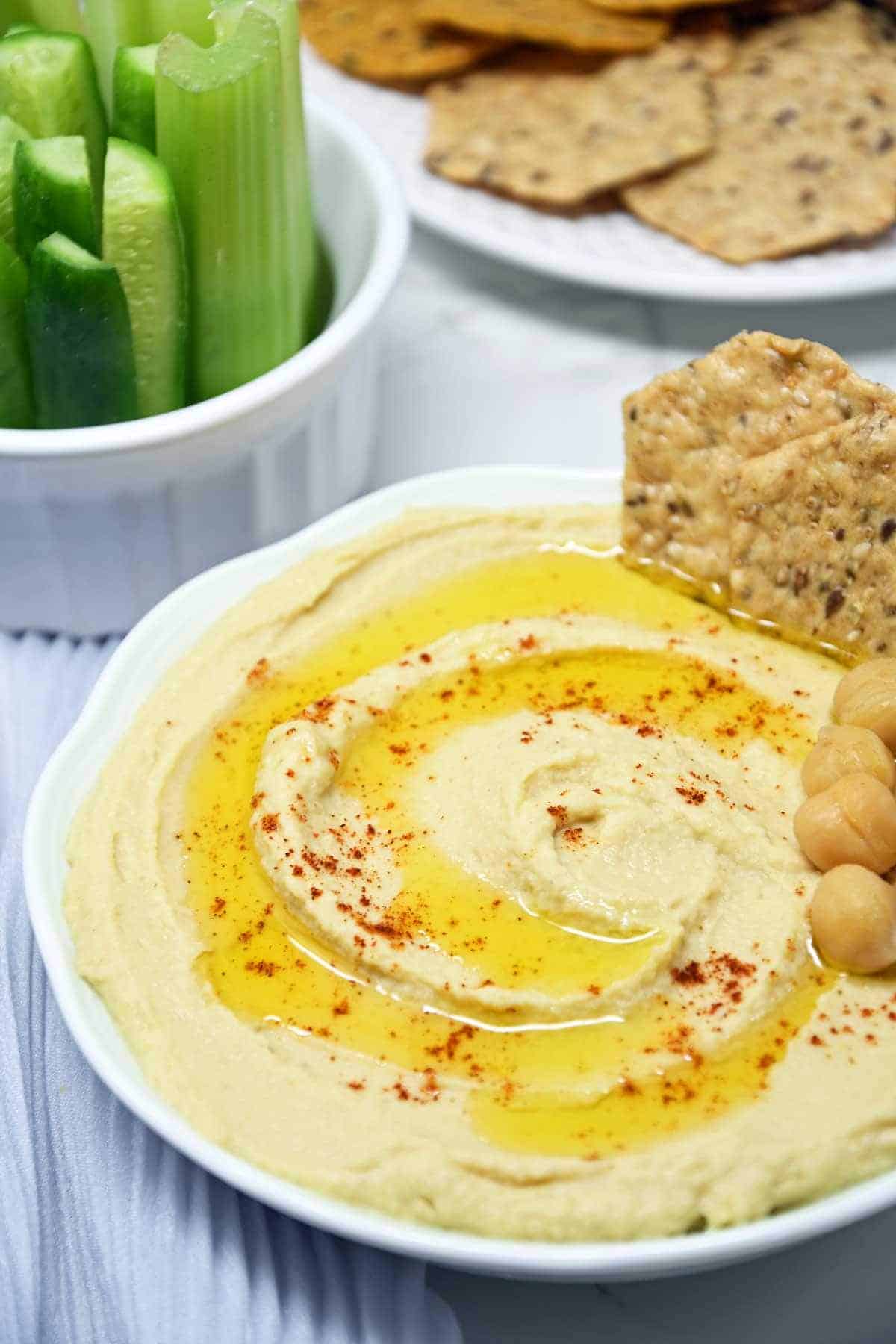 Oil drizzled over instant pot hummus with a cracker and chickpeas garnished on the side. 