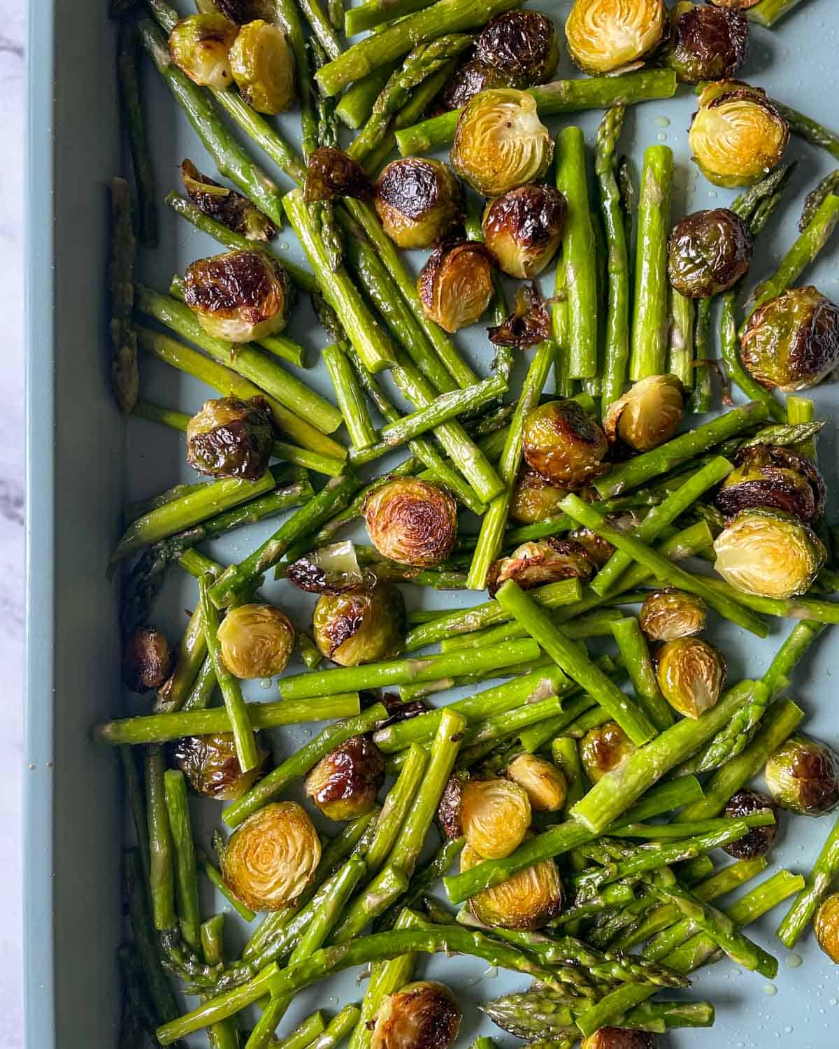 Roasted brussels sprouts and asparagus in a baking pan.