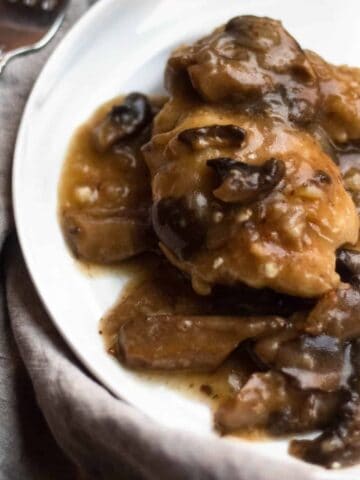 Chicken marsala on a white plate with a linen next to it.