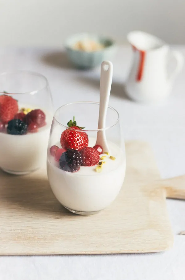 Panna cotta, an Italian dessert recipe, served in small glass cups with fresh berries garnished on top. 