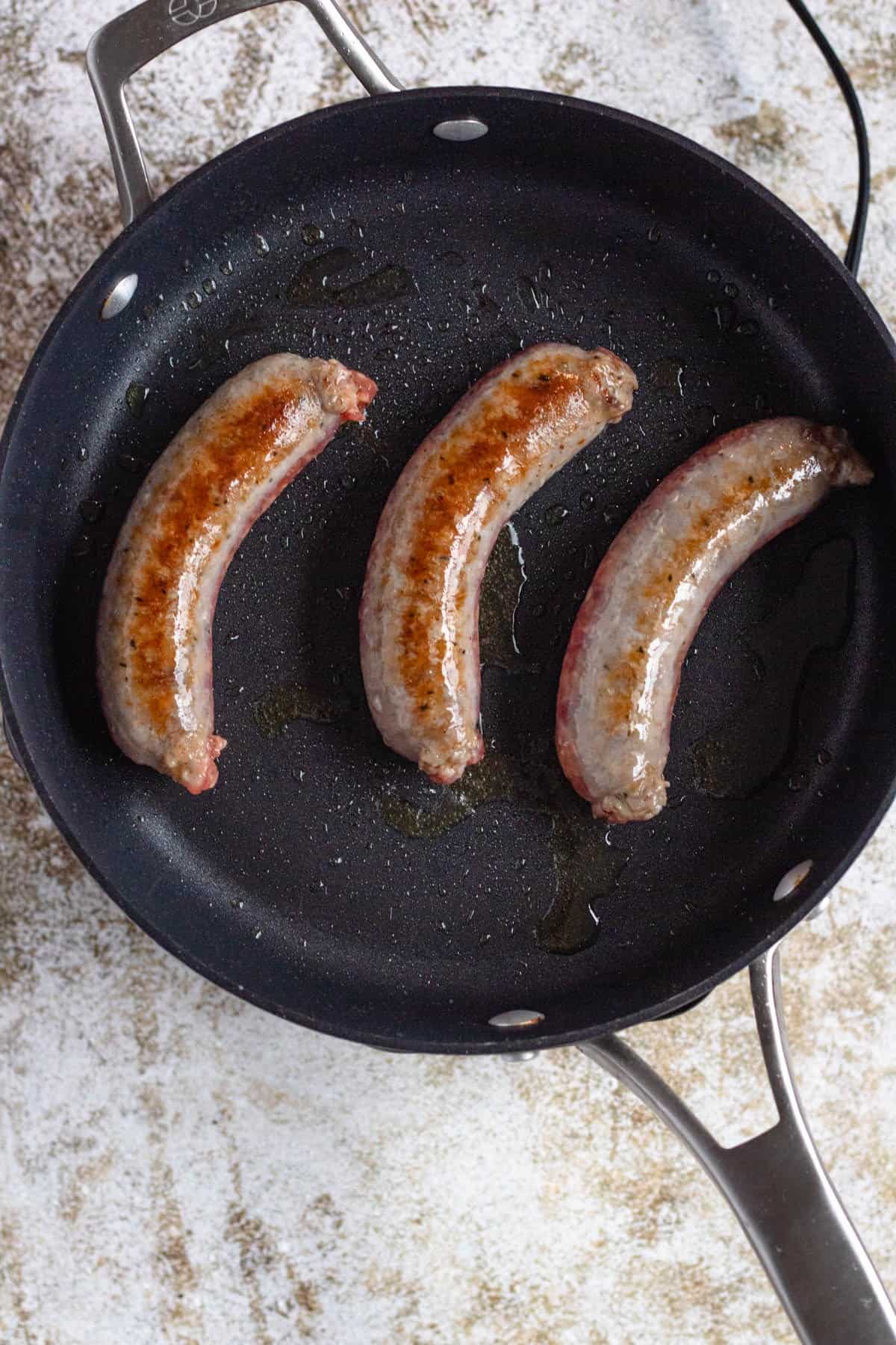 Sausages cooking in a skillet for Italian Sausage and Peppers recipe.