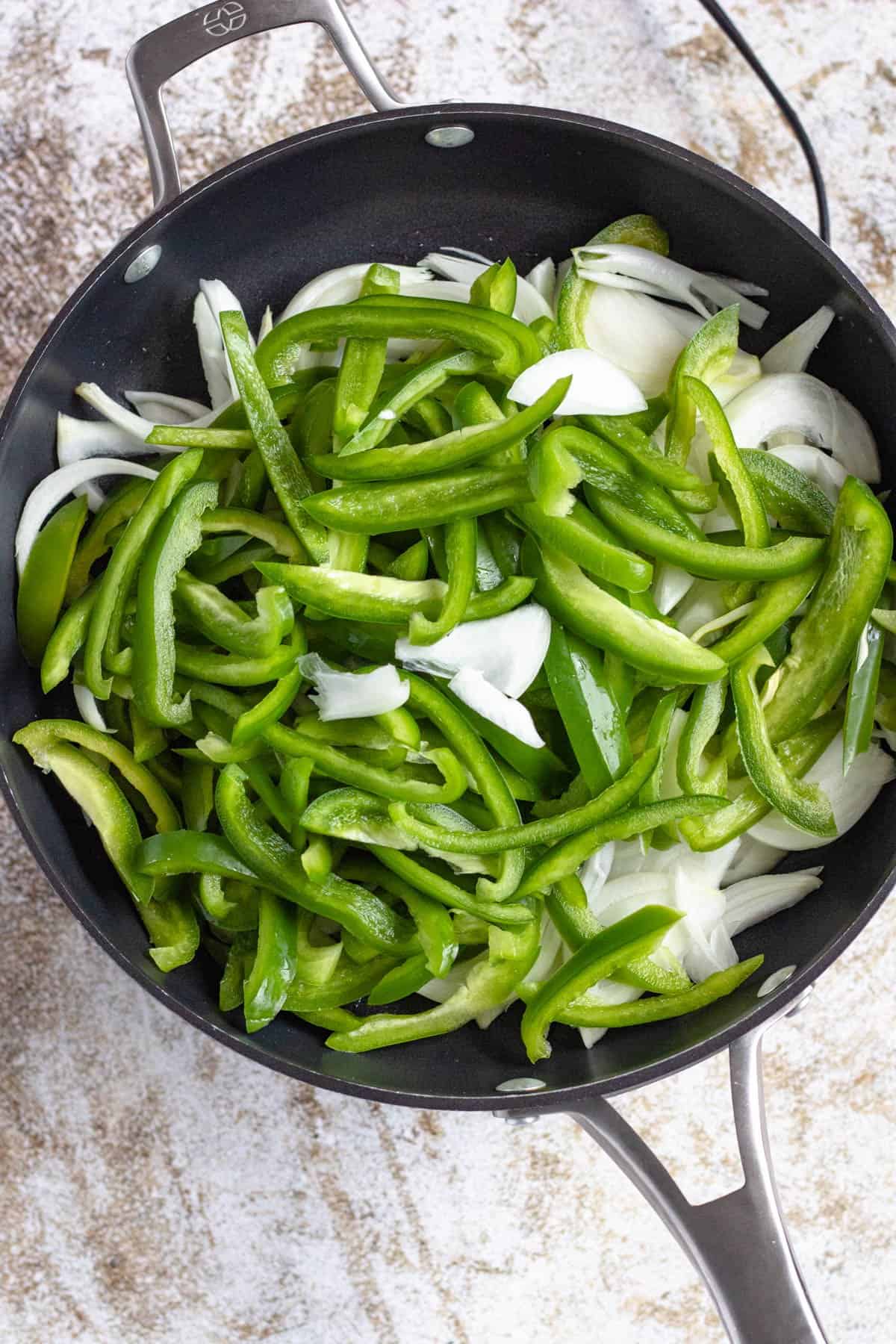 Fresh cut green bell peppers and sliced onions in a skillet. 