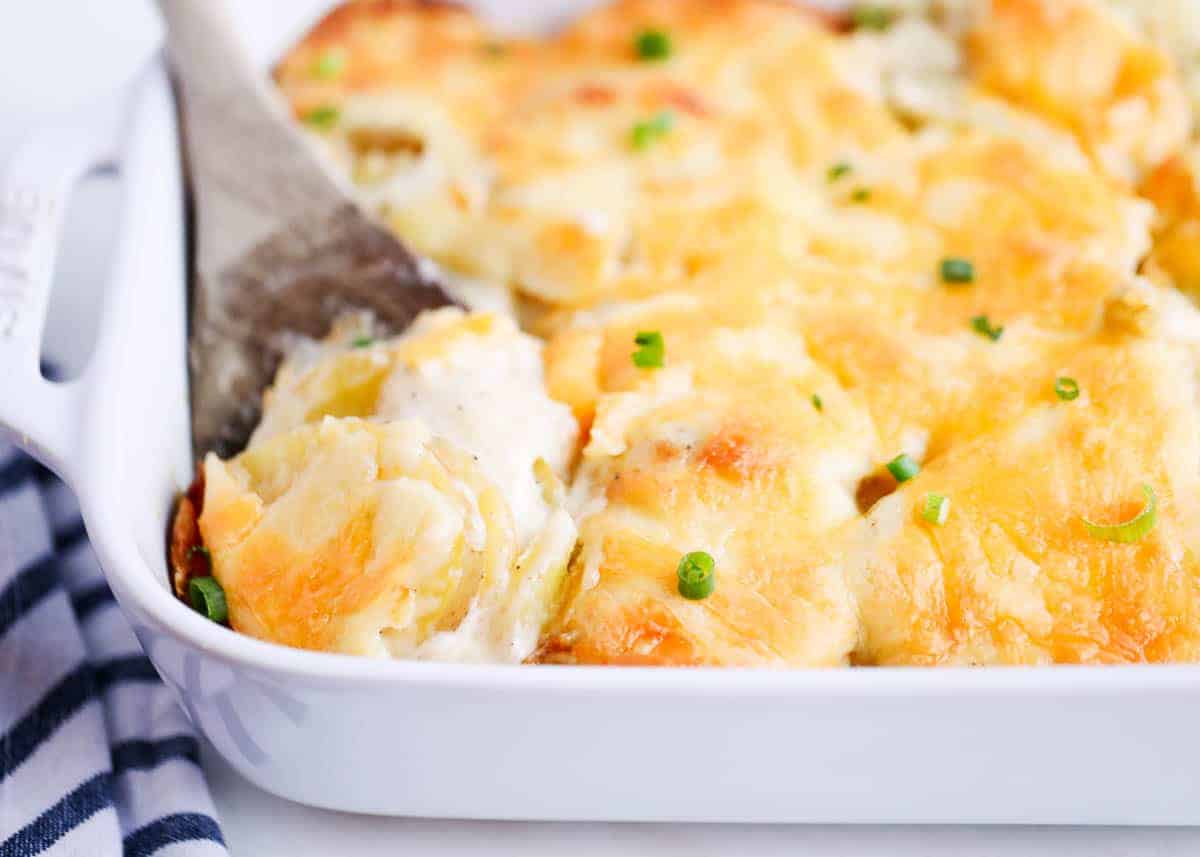 Cheesy Scalloped Potatoes in a baking dish being scooped up. 