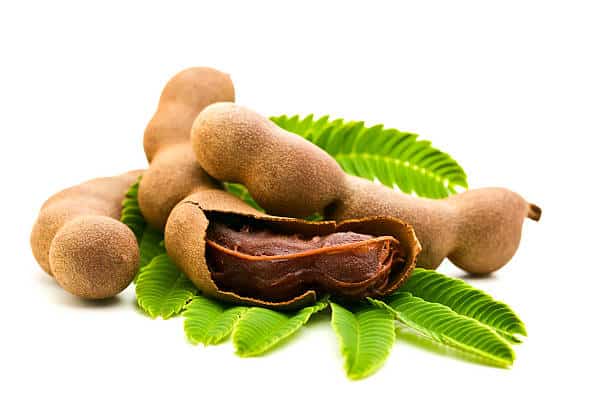 A partially open tamarind and others whole laying on a green leaf. 