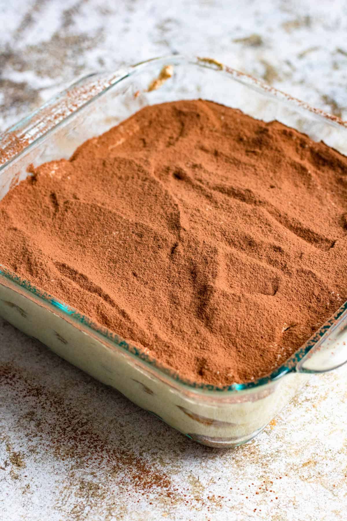 Cocoa powder layered over the top of the mascarpone creamy filling to finish the easy tiramisu recipe. 
