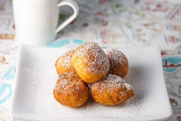 Zeppole, Italian dessert recipe, stacked on a small white plate and dusted with powdered sugar.