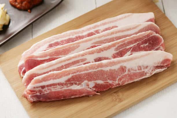 Slices of pork belly on a wooden cutting board. 