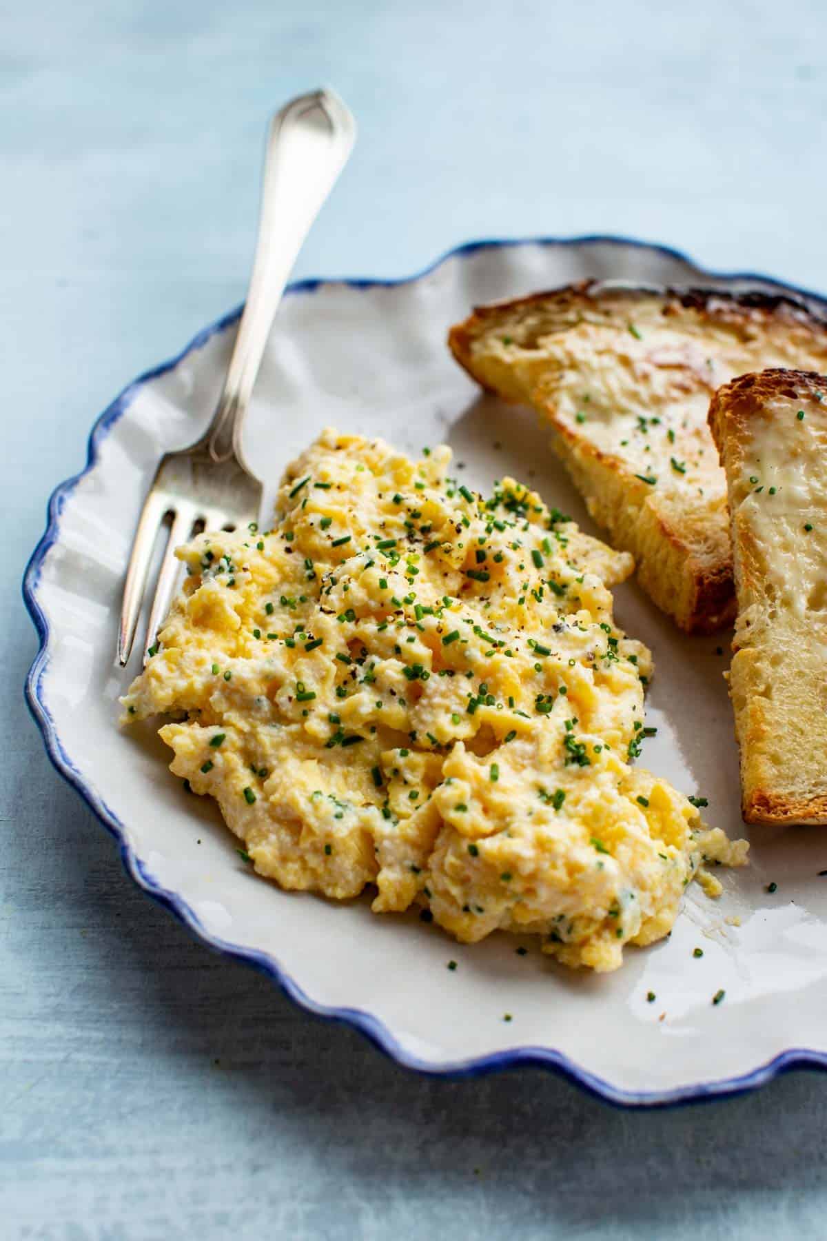 Soft scrambled eggs with ricotta on a plate with 2 pieces of toast. 