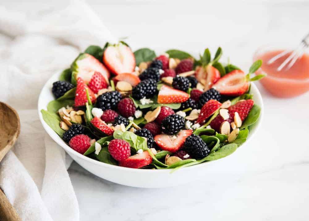 Spinach berry salad in a bowl next to a the vinaigrette. 
