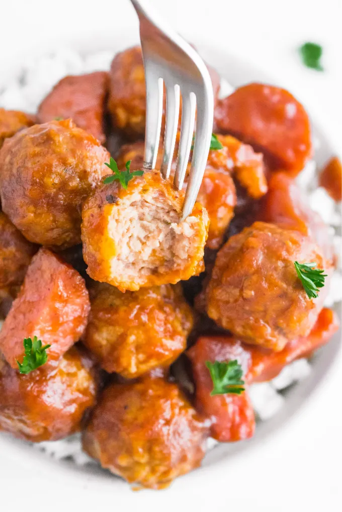 Fork stuck in a crockpot cranberry meatball laying in a bed of rice. 