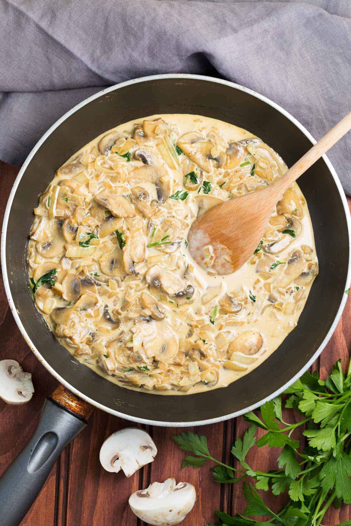 Creamy garlic mushrooms in a skillet with a wooden spoon laying in it. 