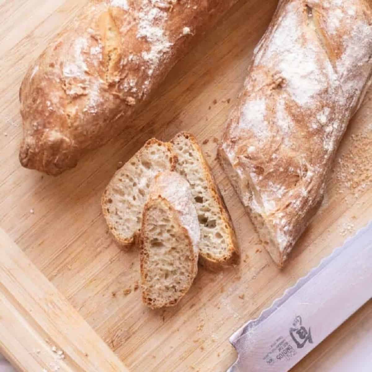 Easy crusty french baguette on a wooden cutting board with a few slices cut off. 