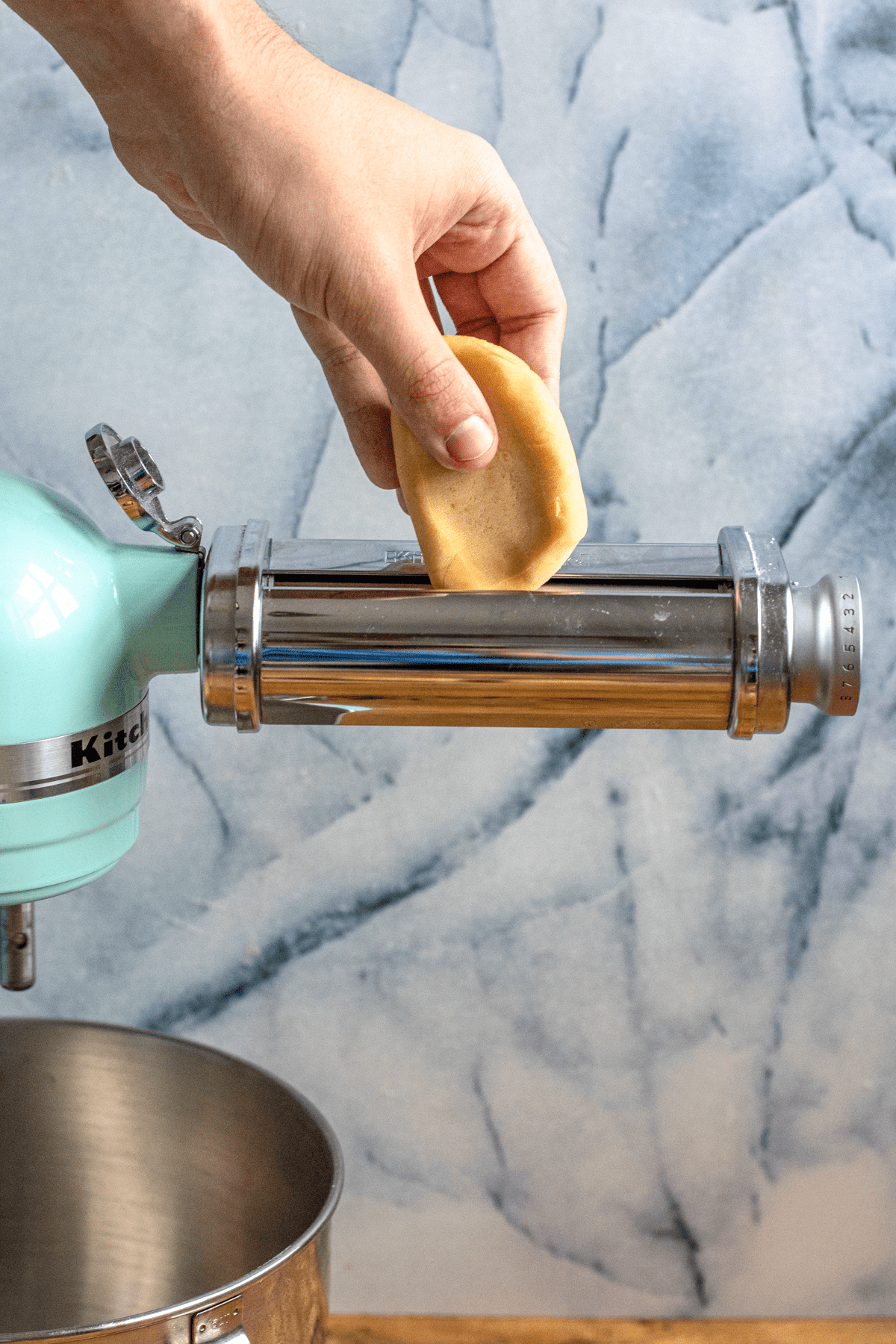 A piece of pasta dough going into a pasta maker. 