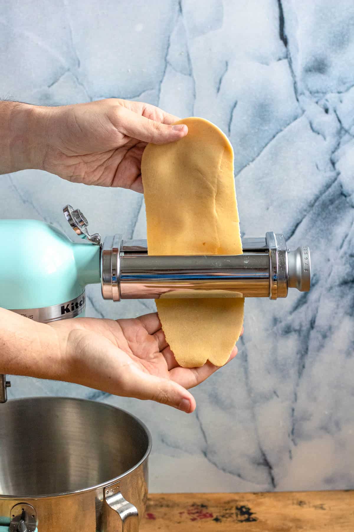 Hand running pasta dough through pasta machine to make ravioli pasta. 