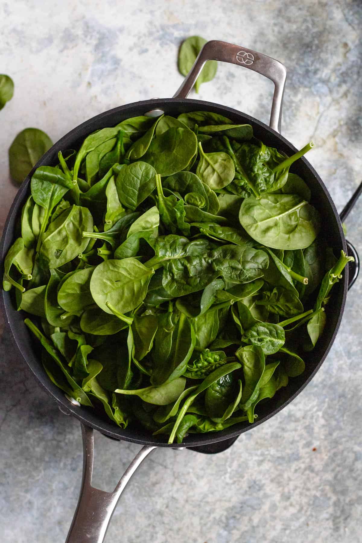 Fresh baby spinach added to a skillet to make ravioli filling recipe. 