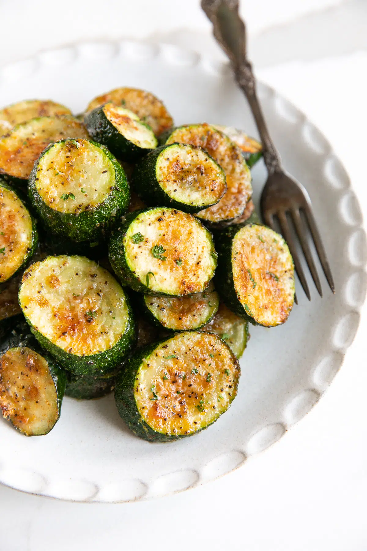 Roasted zucchini slices on a plate with a fork laying next to it. 
