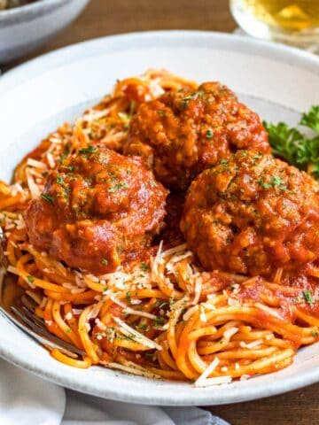 Soft meatballs served over a bed of spaghetti sprinkled with parsley.