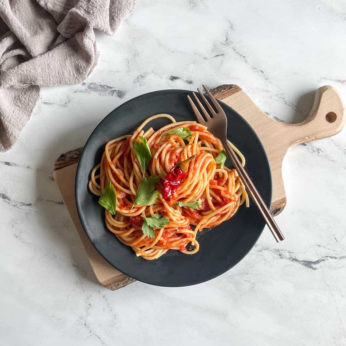 Spaghetti arrabbiata with a fork on a plate and fresh parsley garnished on top. 