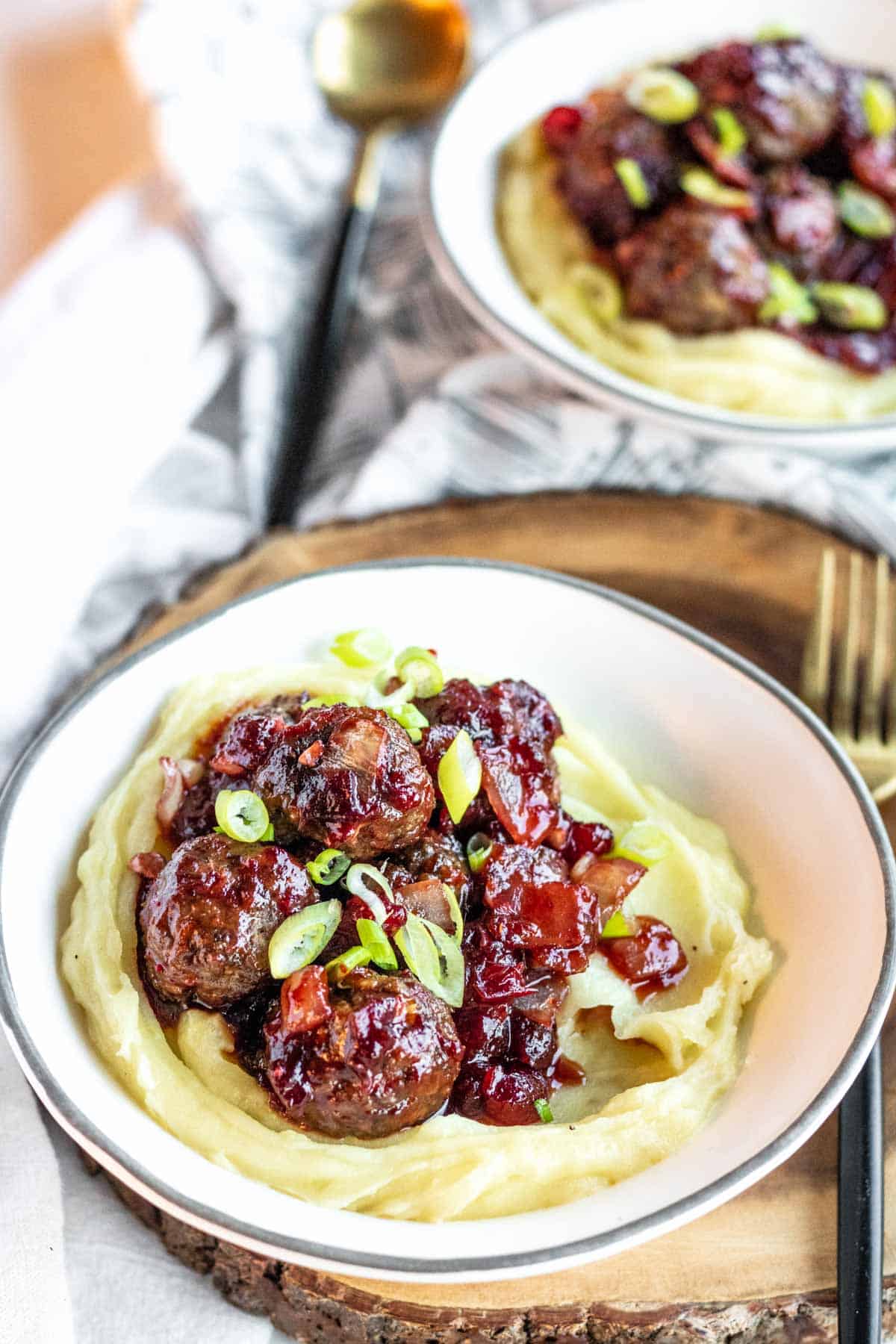 Orange cranberry meatballs served over mashed potatoes in a bowl and garnished with green onions. 