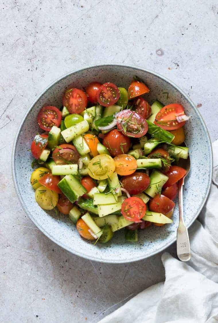 A spoon inside a bowl of cucumber tomato salad. 