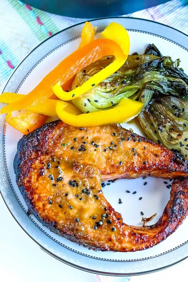 An air fryer salmon steak on a plate with cooked veggies. 