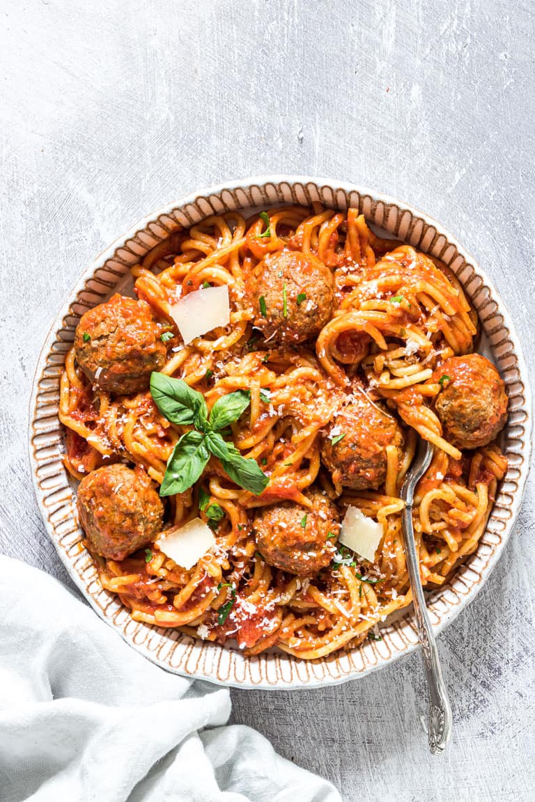 Bowl of spaghetti and meatballs with a basil garnish. 