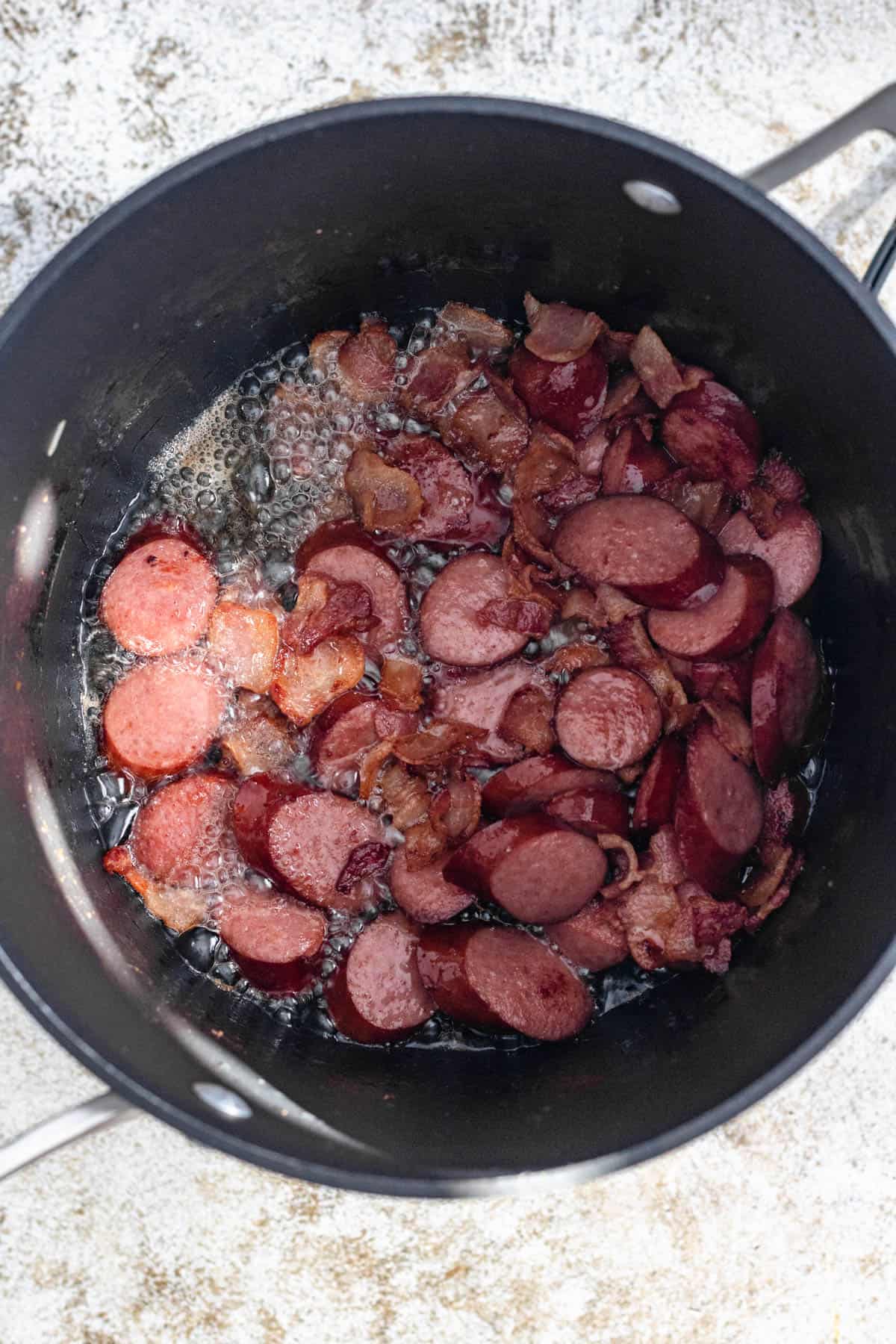 chorizo and sausage frying in a saucepan. 