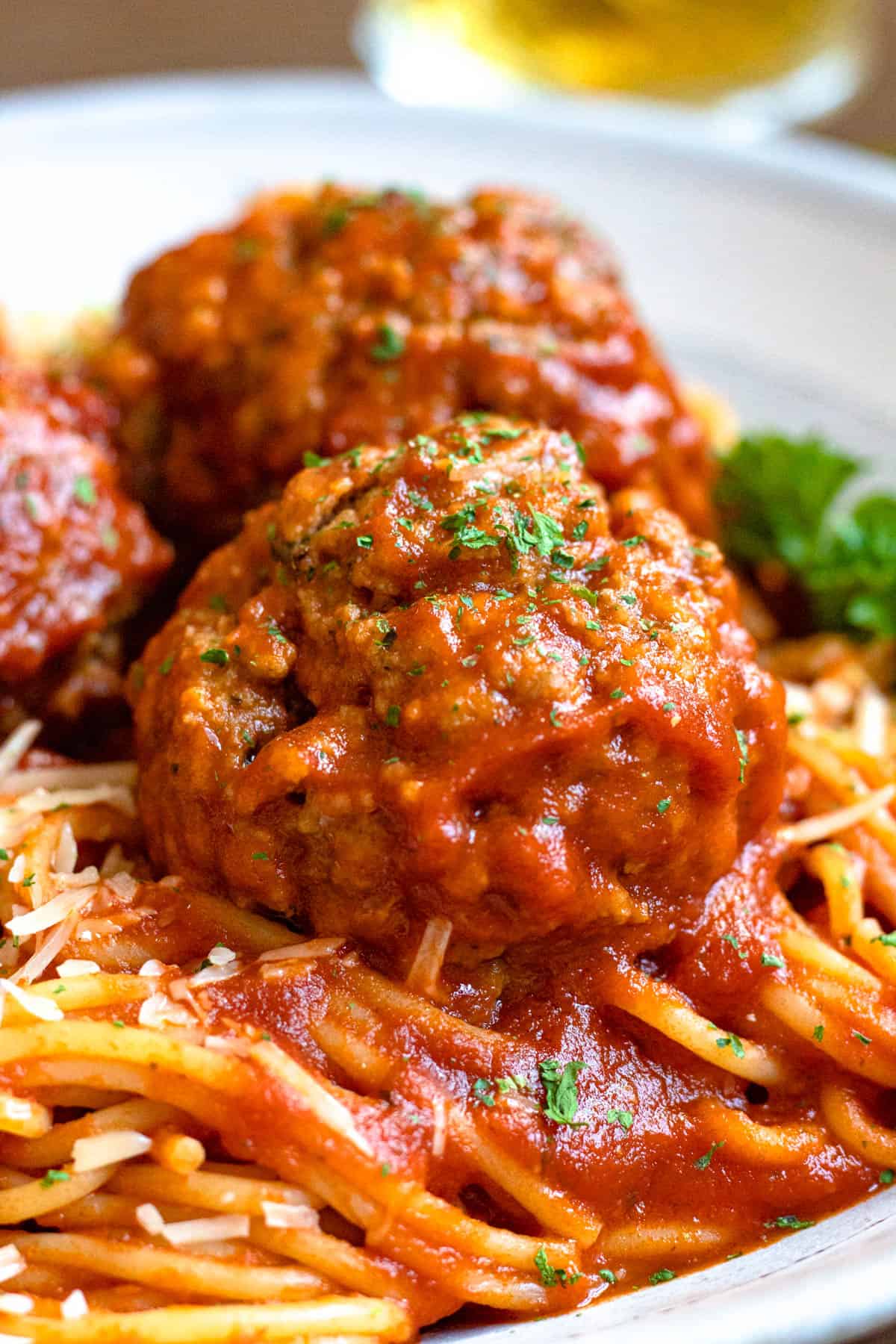 Close up of soft meatballs recipe covered in tomato sauce and served over a bed of pasta. 