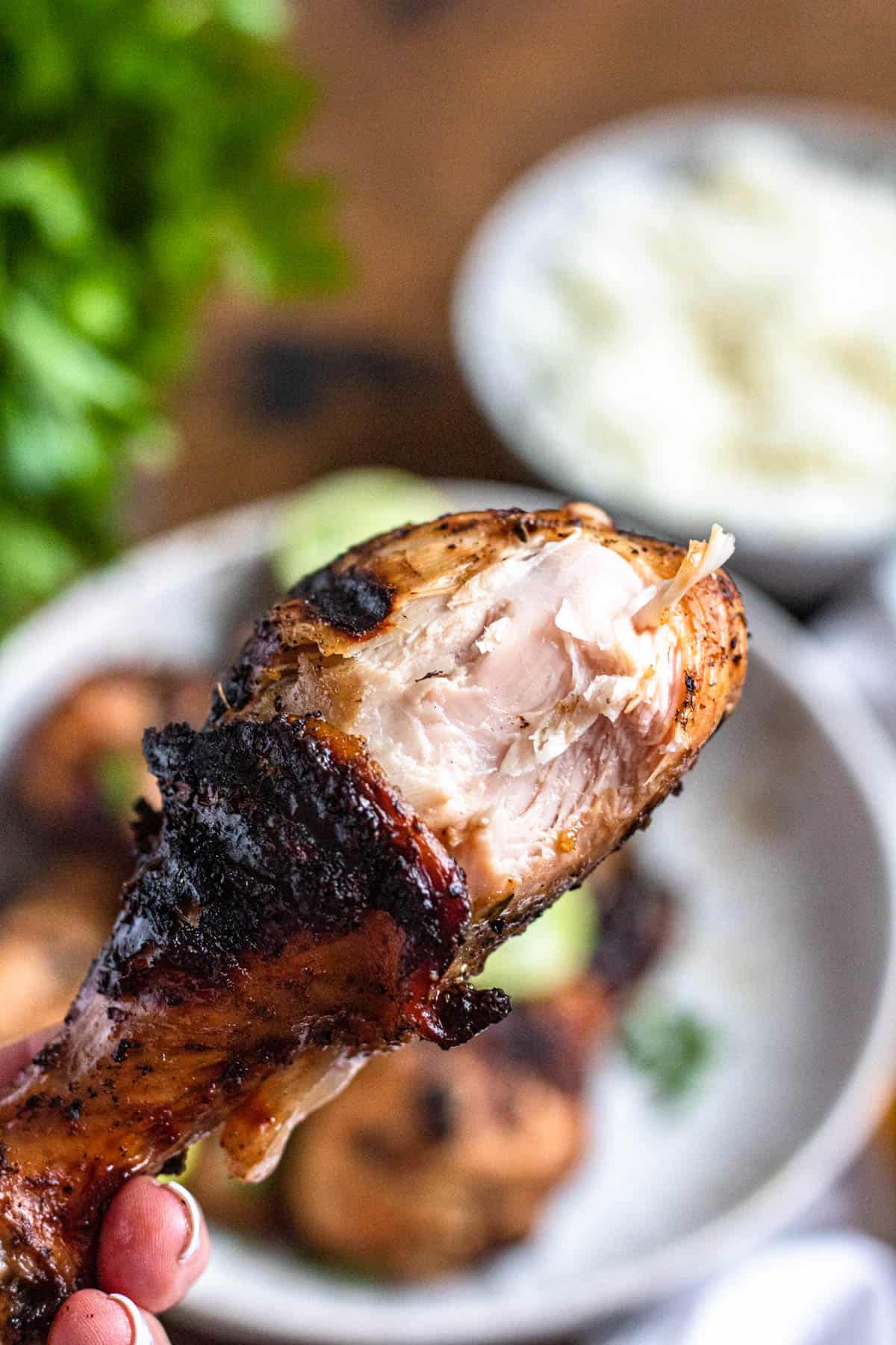 Hand holding up a jerk chicken drumstick with a bite missing. 