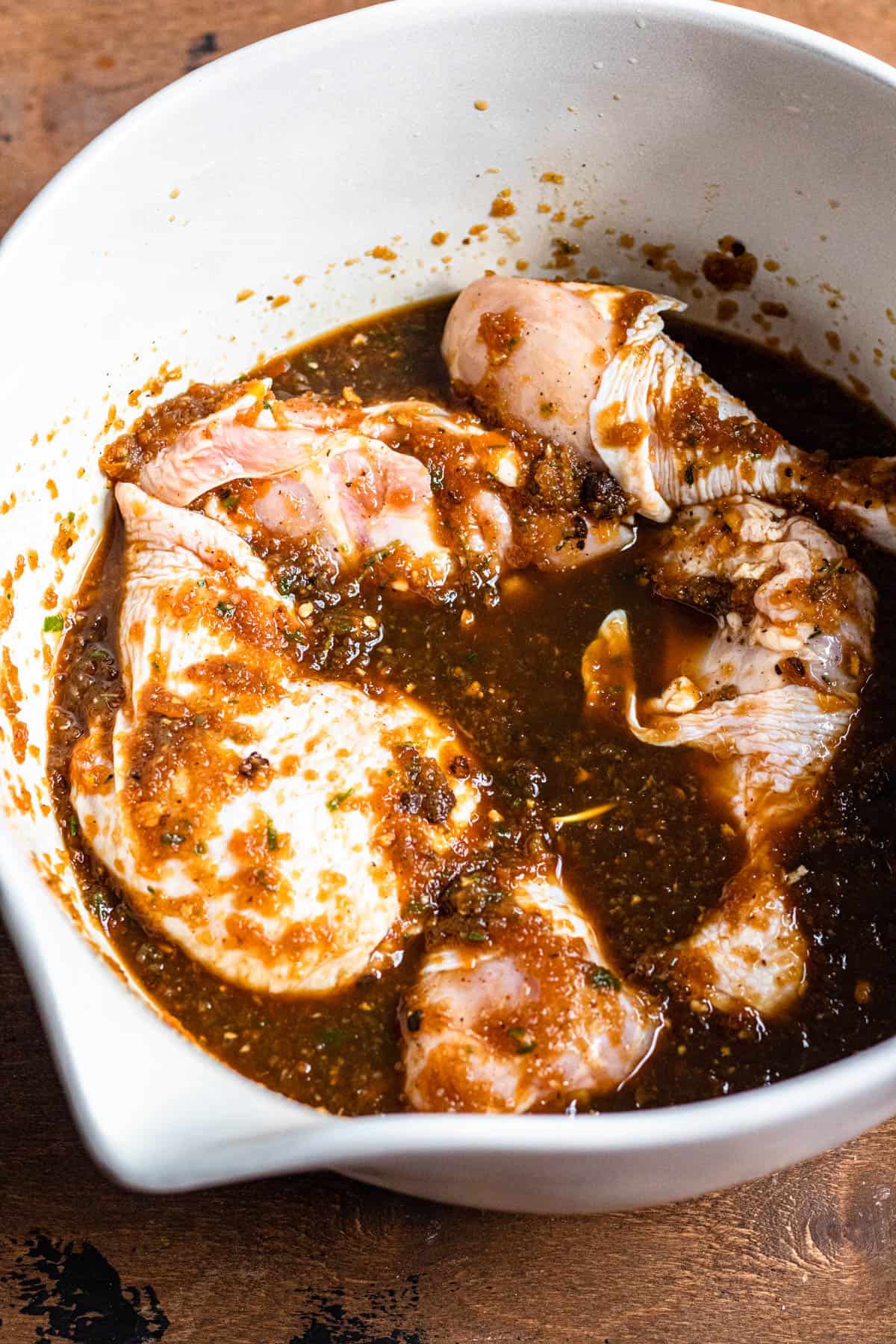 Raw bone-in chicken in a mixing bowl topped with the jerk marinade. 