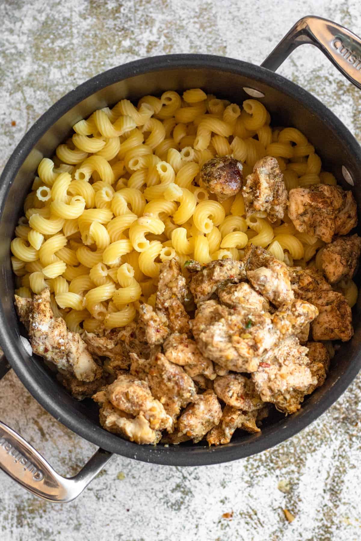 Cooked cavatappi pasta with cooked jerk seasoned chicken in a saucepan. 