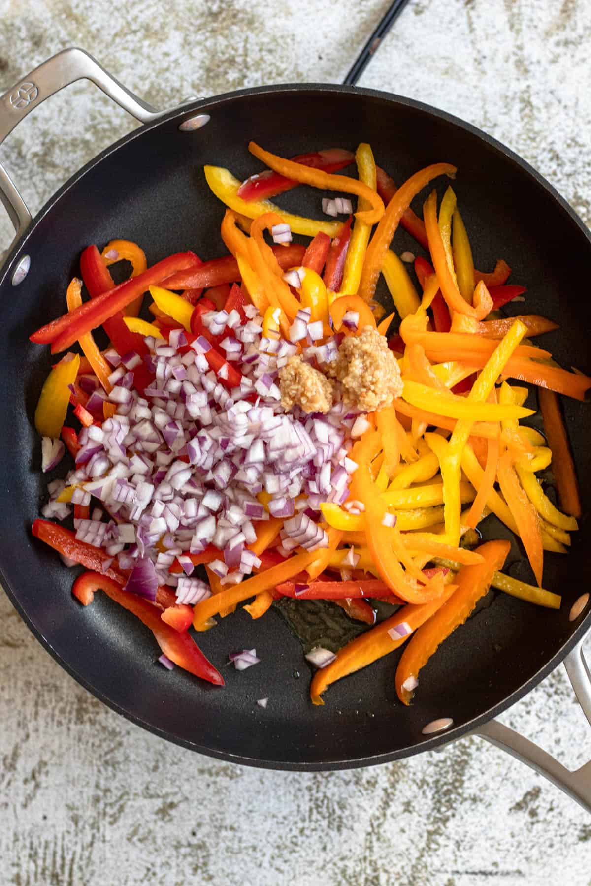 Skillet with sliced bell peppers and diced red onion with garlic. 