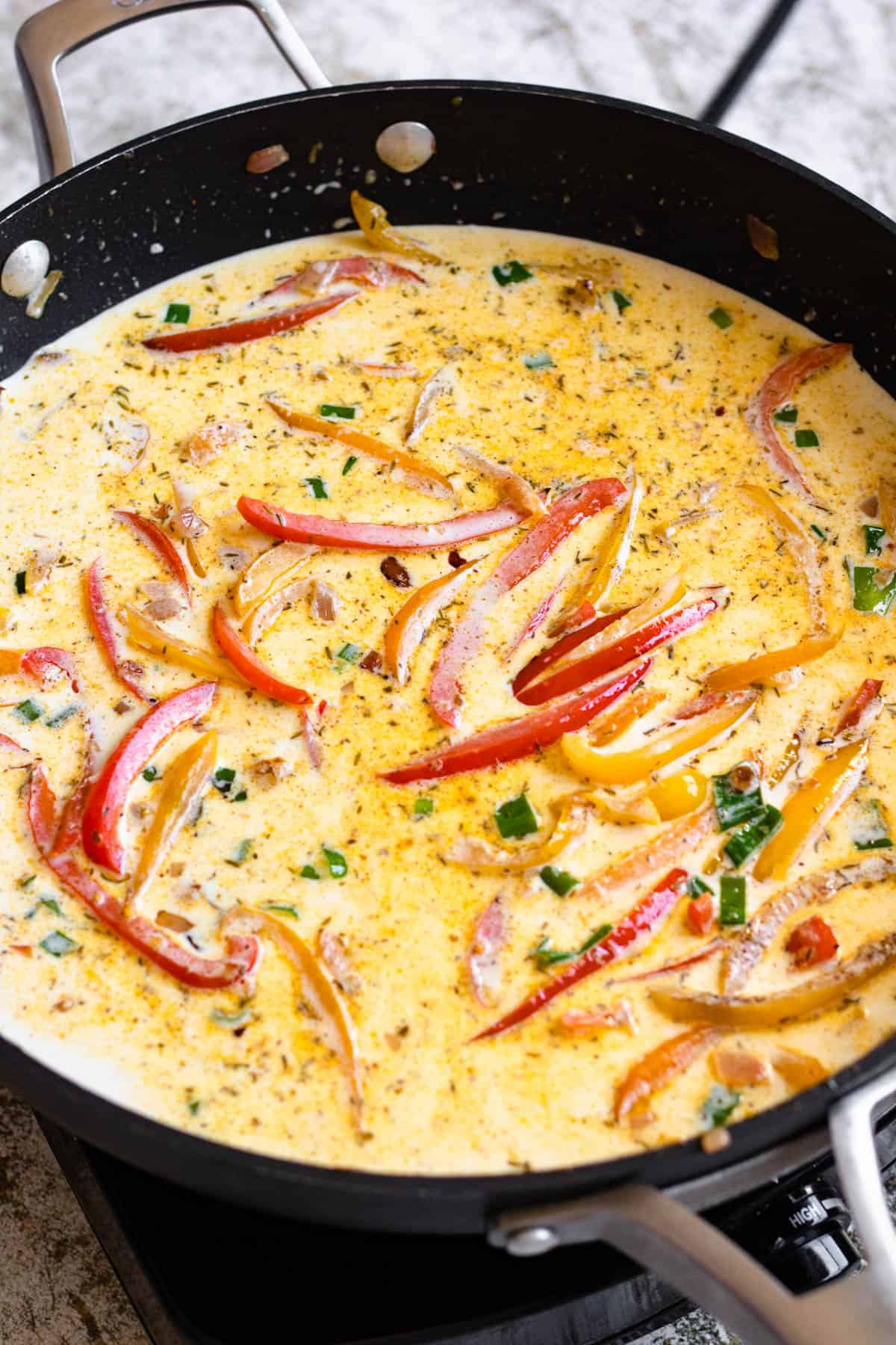 Cream sauce and bell peppers in a skillet. 