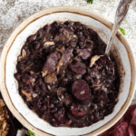 Pinterest image of a top view of a bowl of Feijoada with a spoon resting in it.