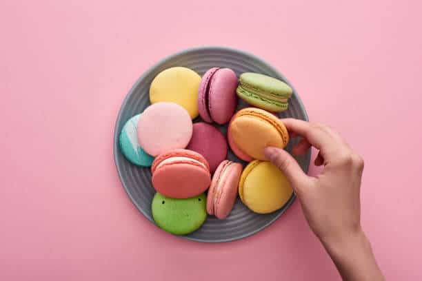 Hand picking up a colorful macaron from a plateful. 