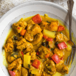 Pinterest image of a top view of a bowl of Jamaican curry chicken with a spoon rest in it.