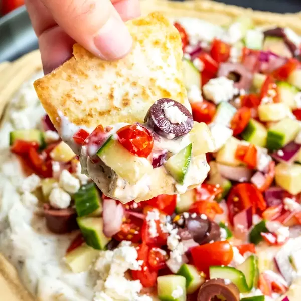 Hand dunking a pita chip into a 5 layer Greek dip. 