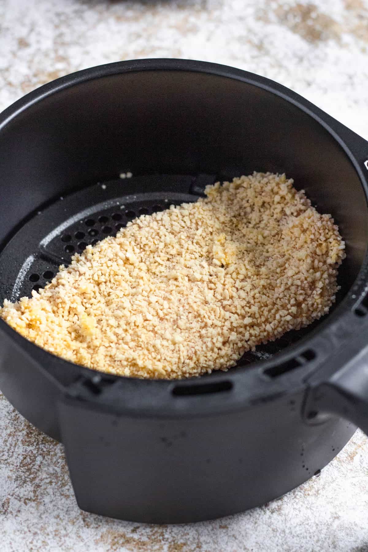 Raw panko breadcrumb coated chicken katsu laying in the air fryer bucket. 