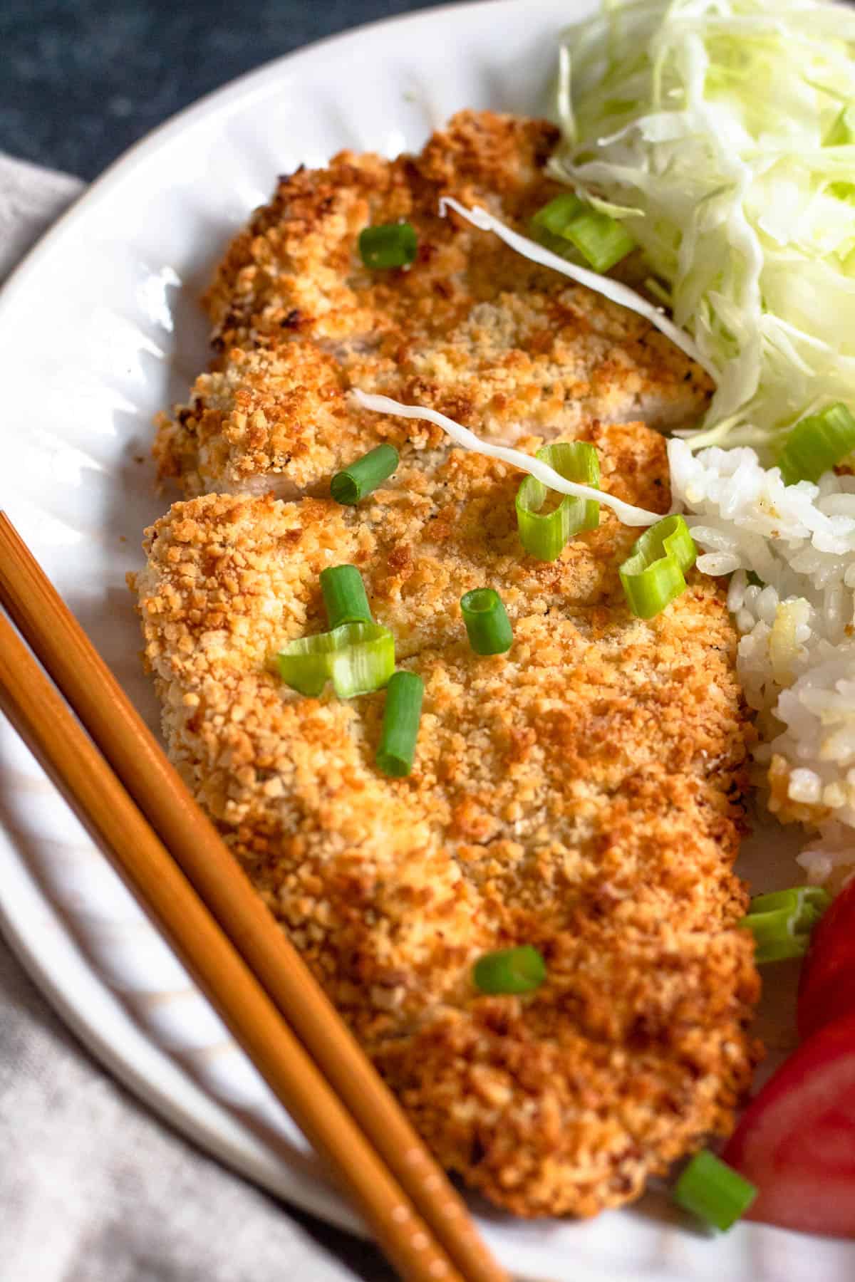 Close up of Chicken katsu sliced into thin pieces on a plate served with white rice. and chopsticks resting on the plate with it. 