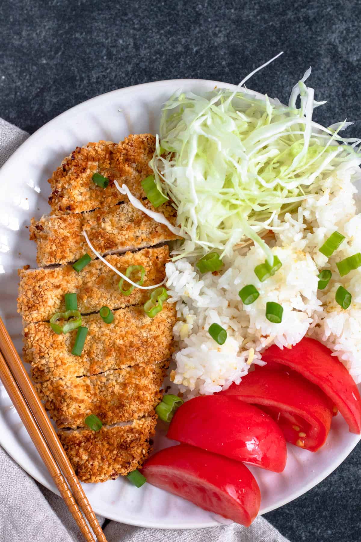 Chicken katsu sliced into thin pieces, served with tomato wedges, white rice and cabbage and garnished with green onions. 