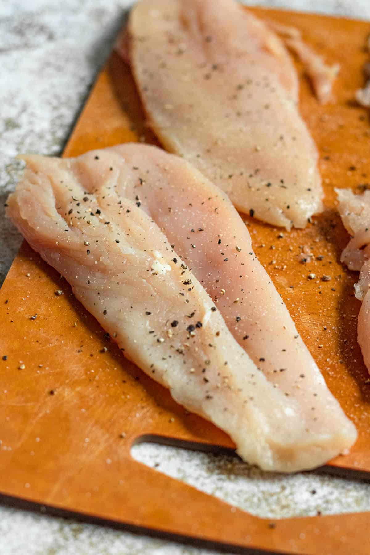 Thin halves of a chicken breast seasoned with salt and pepper. 