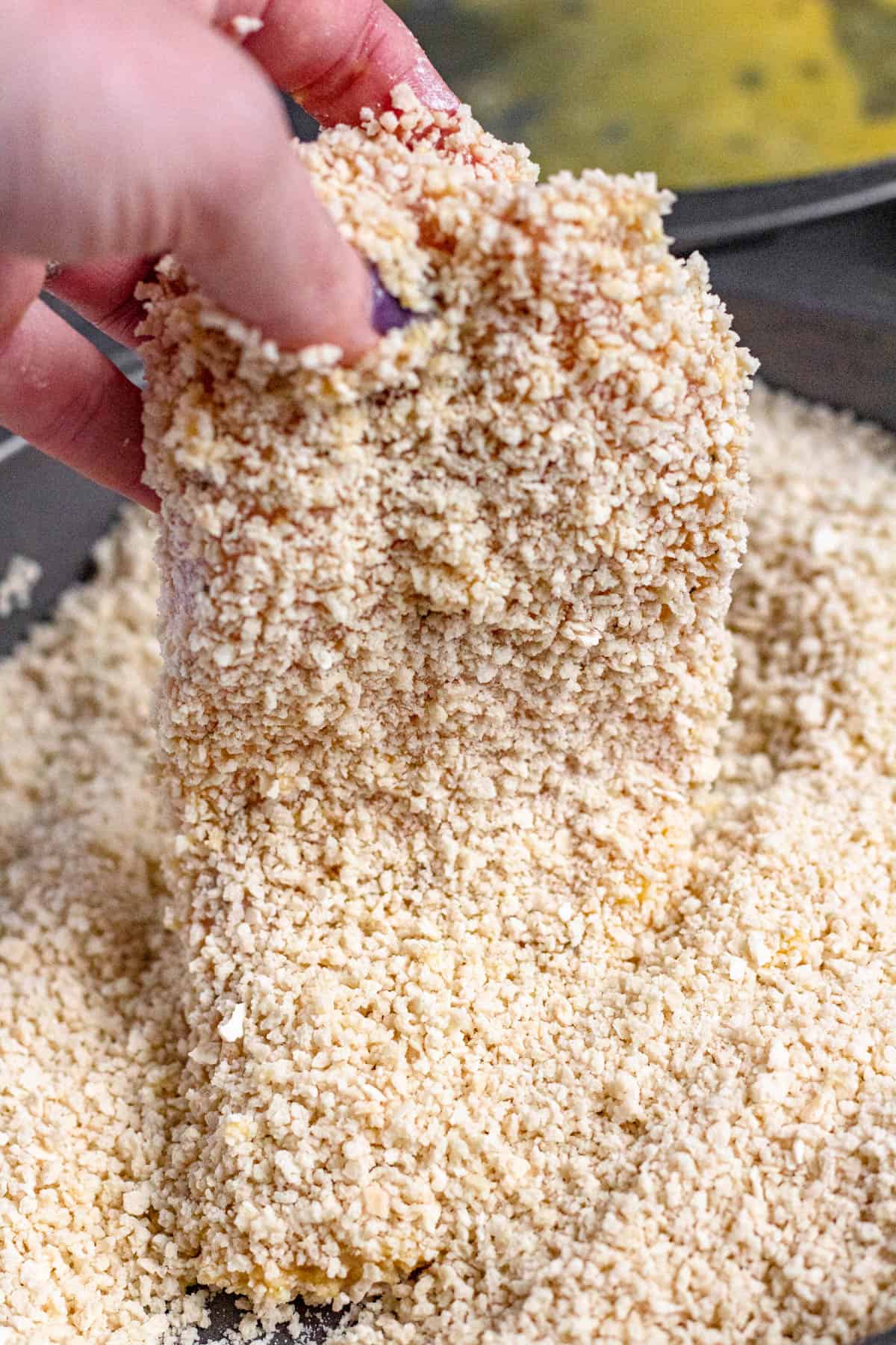 Panko breadcrumbs covered chicken breasts being picked up. 