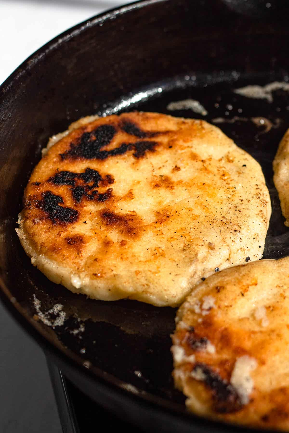 Golden brown arepas in a cast iron pan. 