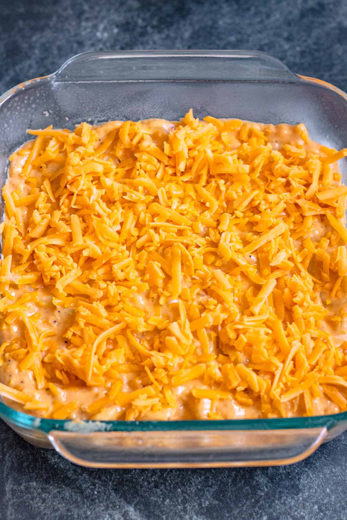 Macaroni added into a glass dish and topped with shredded cheese. 