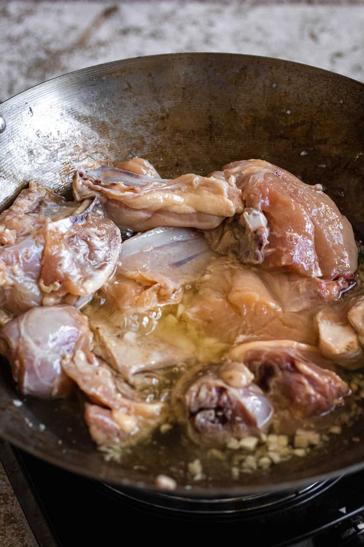 Chicken pieces added to the garlic in the wok. 