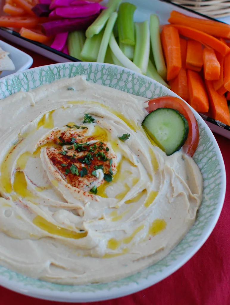 Lebanaese Hummus with a drizzle of oil in a bowl with a cucumber and tomato slice garnished on the side. 