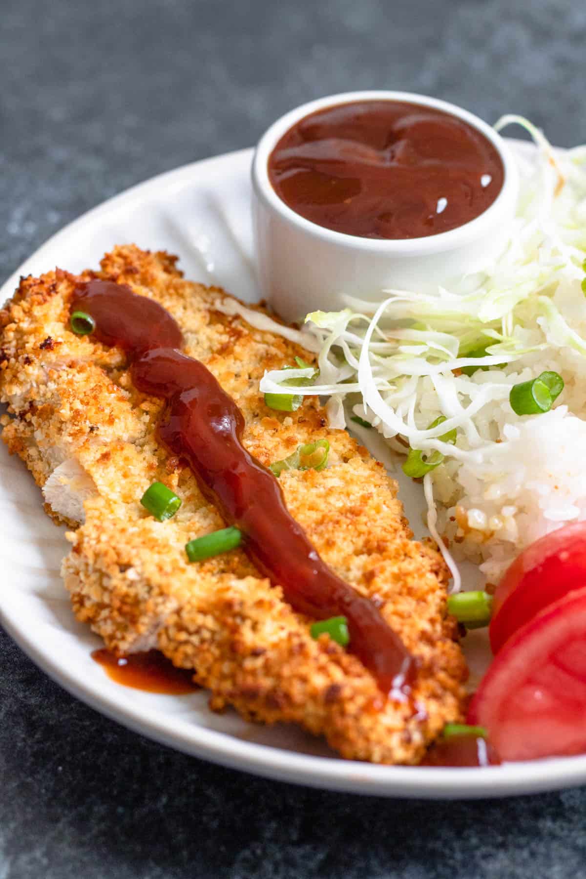 Chicken Katsu with katsu sauce added to the top of it as well as a small bowl of easy katsu sauce on the plate. 